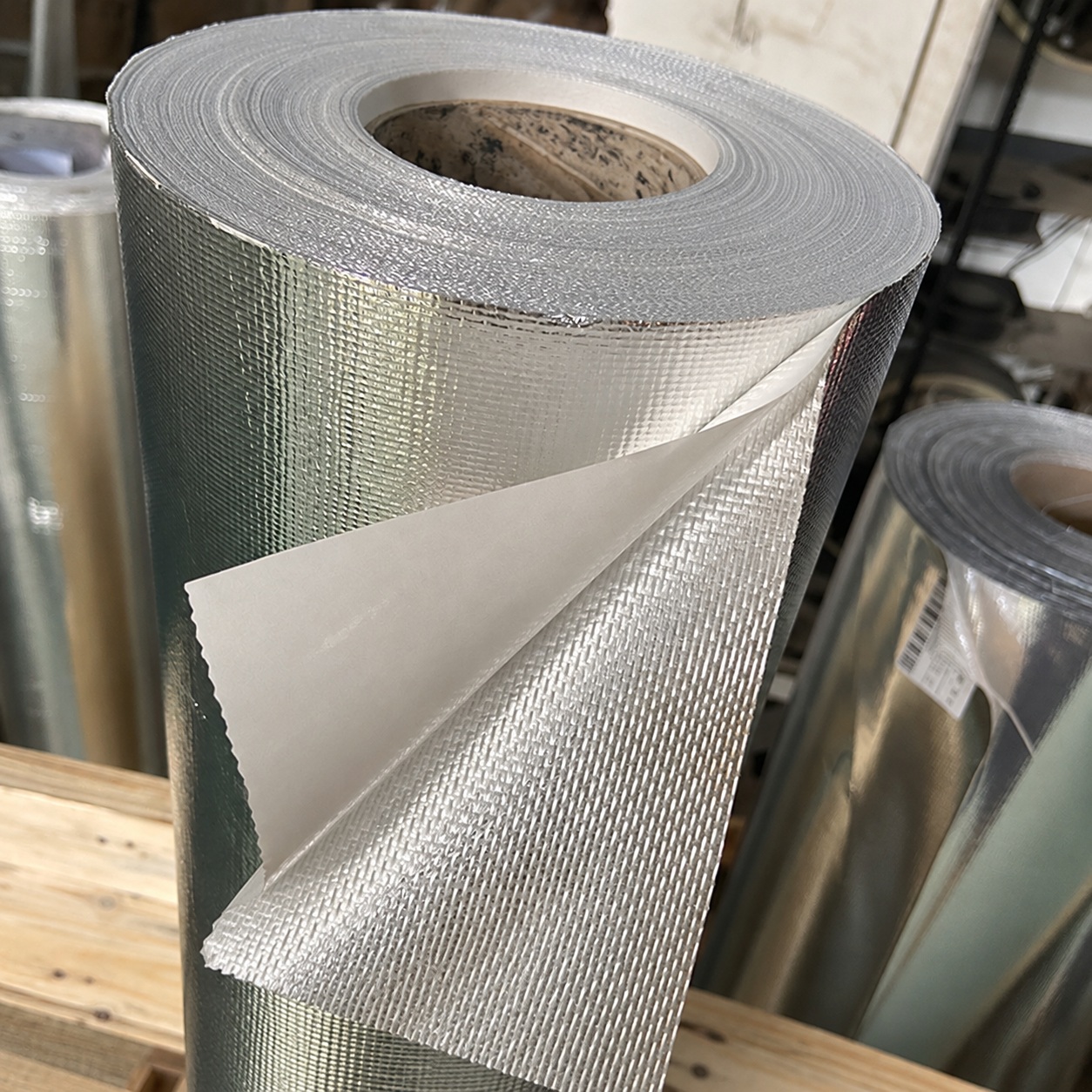Roll of silver foil-faced woven fabric with a pale backing folded forward.