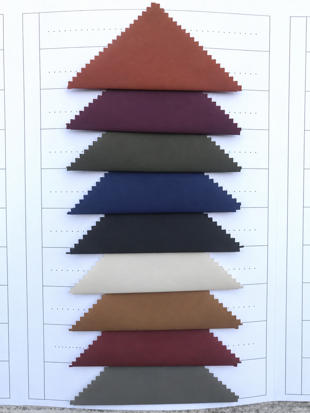 Nine colored triangular fabric swatches arranged vertically on a gridded sample card.
