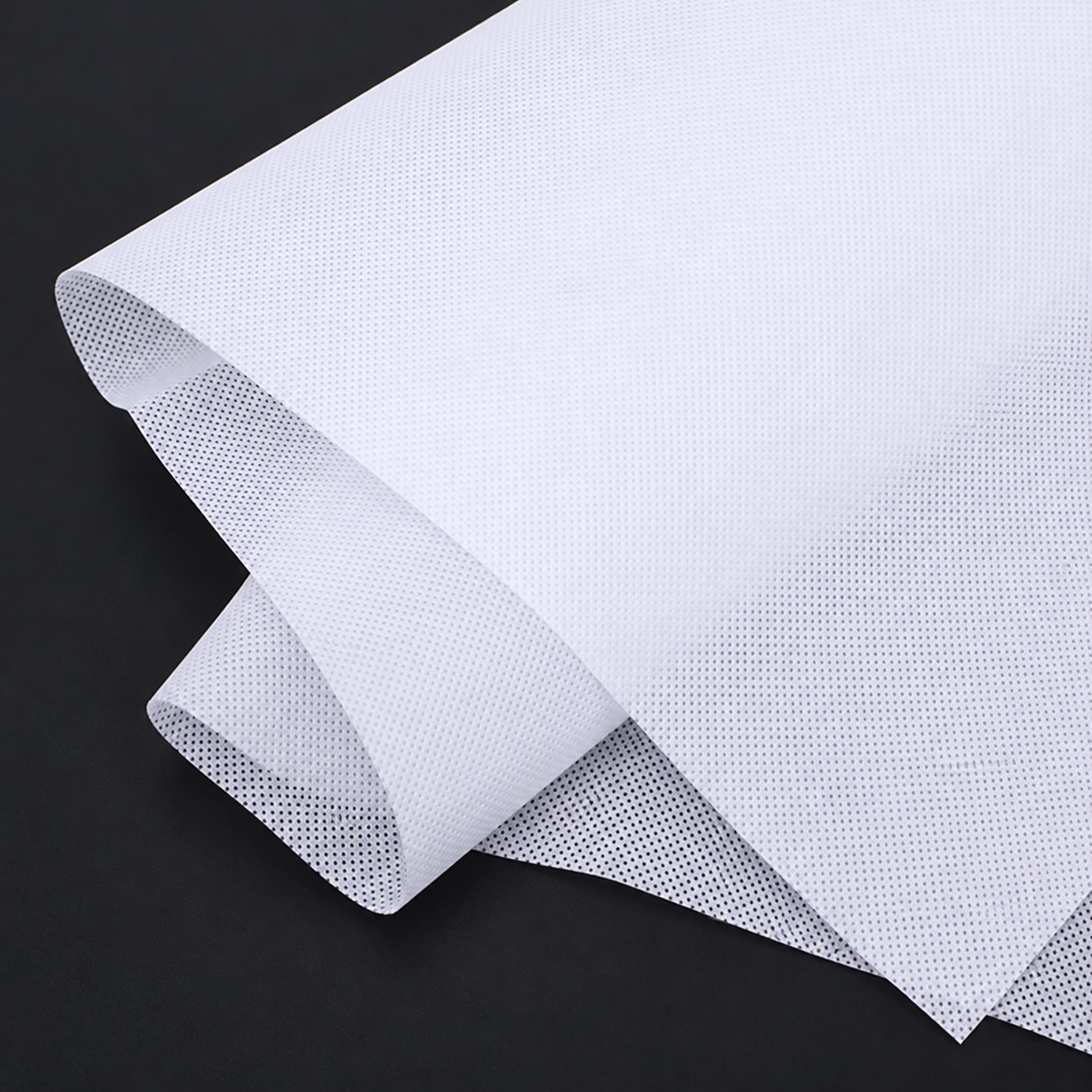 White nonwoven fabric with a regular bonded-dot texture and curled folds.