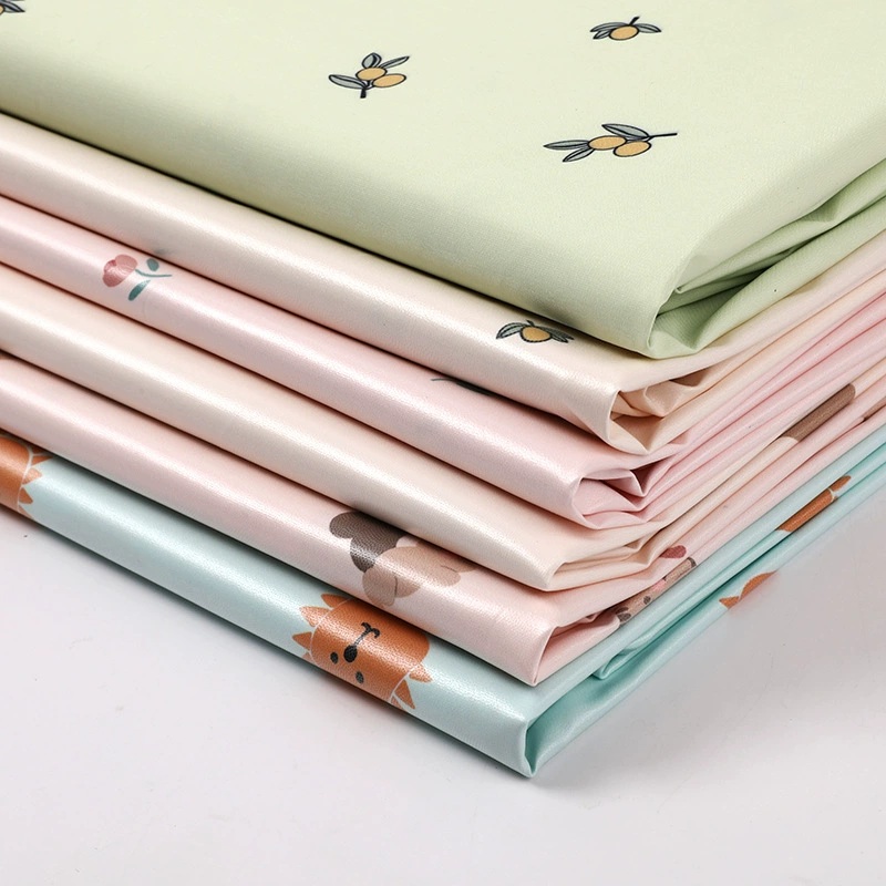 Stacked pastel printed fabric swatches with a pale green fruit-and-leaf print on top.