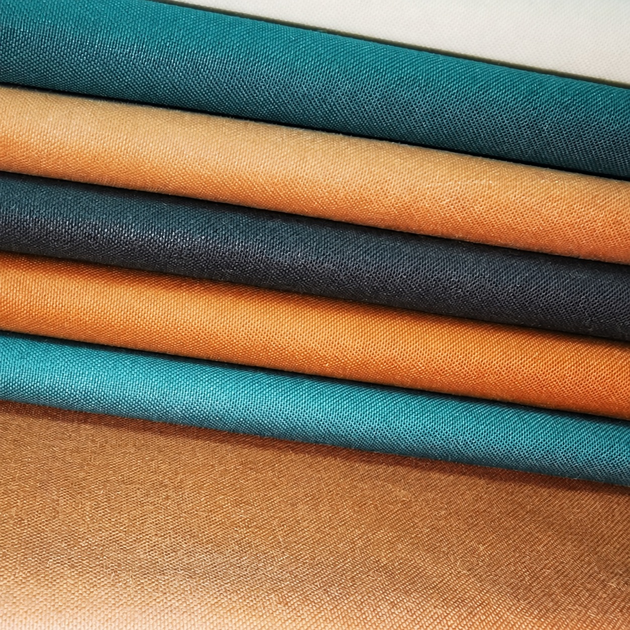 Teal, charcoal and ochre fabric arranged in alternating rolled folds.
