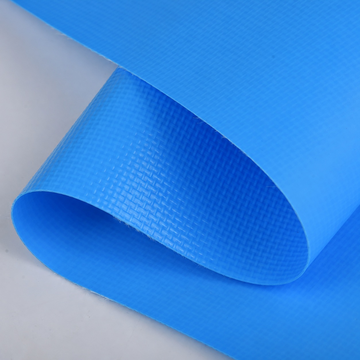 Blue coated woven fabric curled into a broad loop on a gray surface.