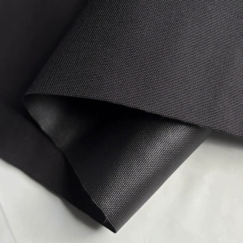 Black woven fabric folded to show its textured face and darker coated reverse.