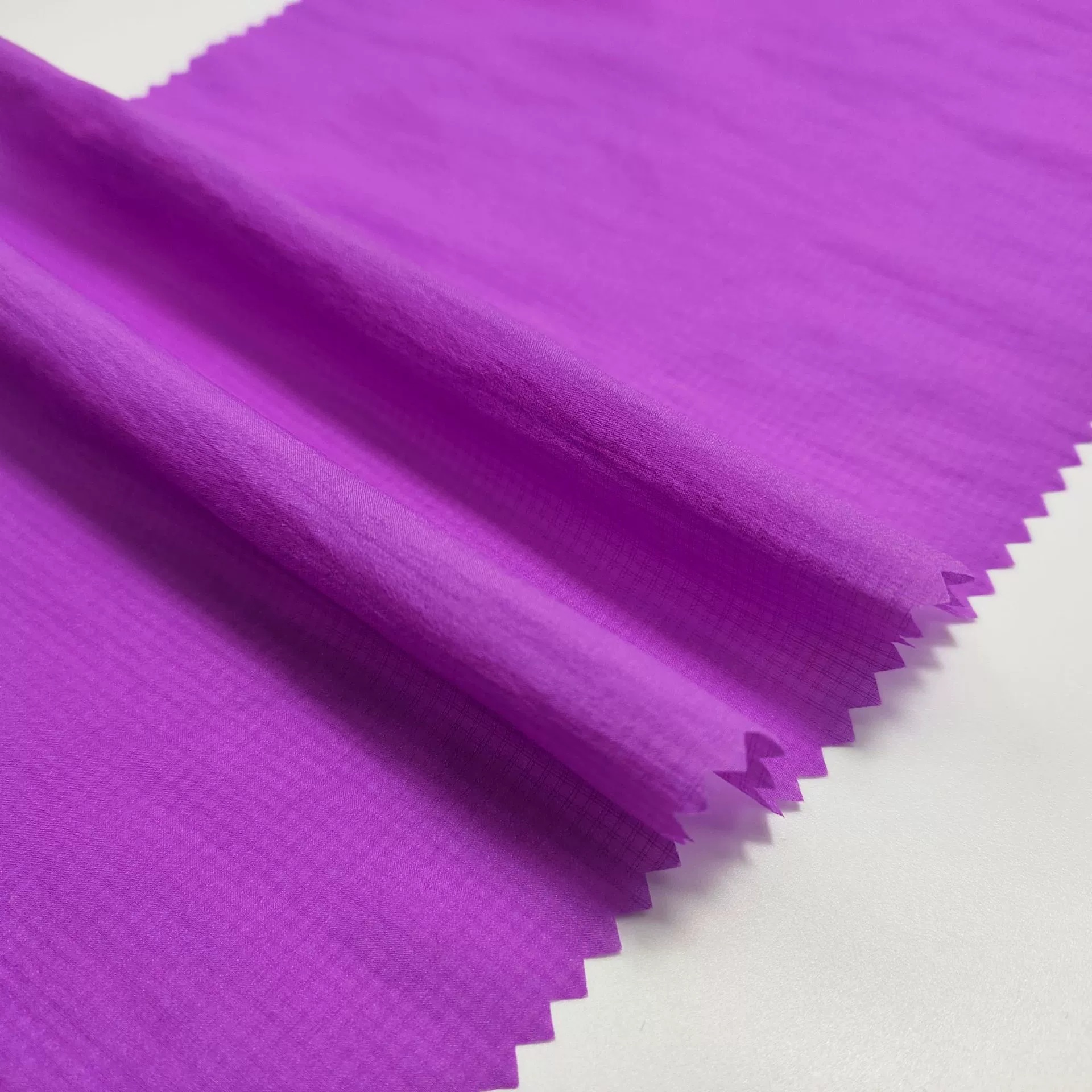 Purple fabric swatches with fine double-line grid texture, soft folds and zigzag-cut edges.