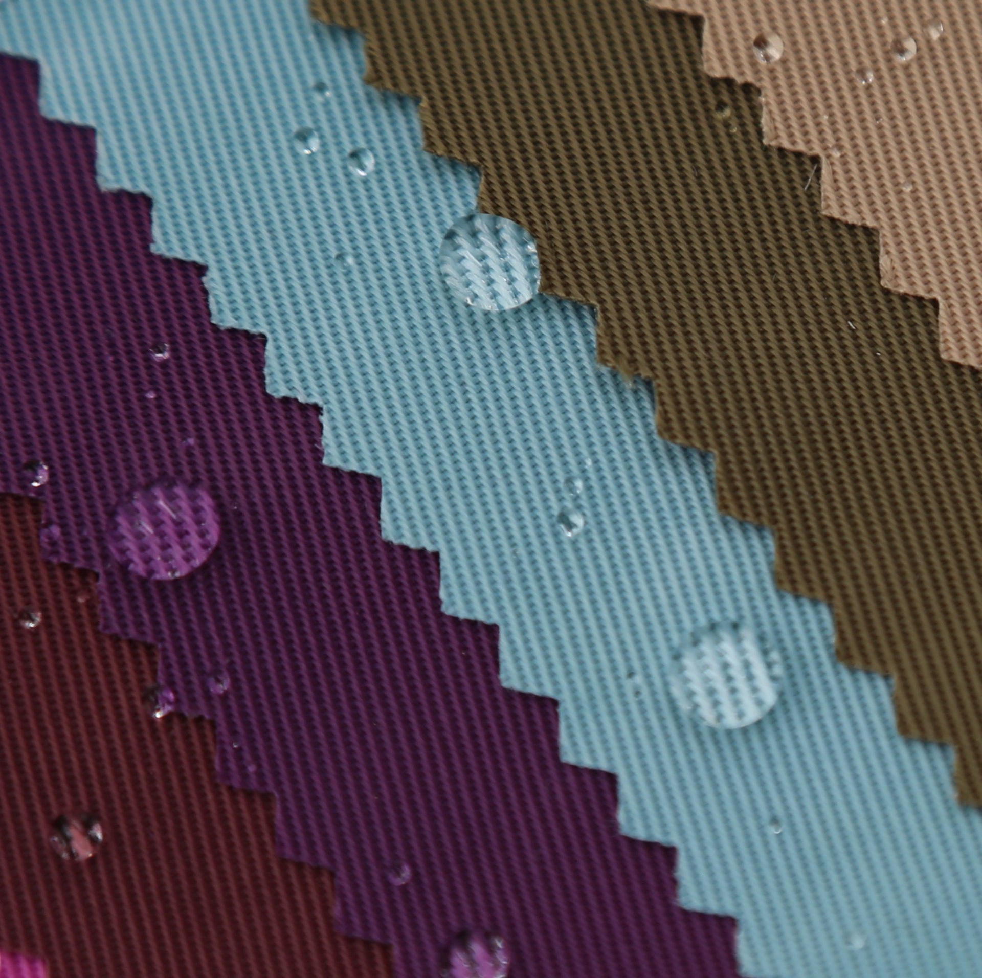 Layered purple, light blue, olive and beige twill fabric swatches with surface droplets.
